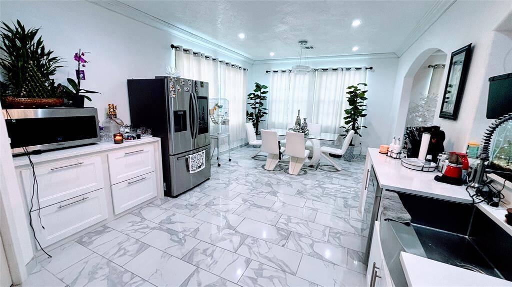 This kitchen features modern white cabinetry, stainless steel appliances, and elegant marble-patterned tile flooring. It includes a sleek range hood, ample counter space, and an open layout with a view into the adjacent living area