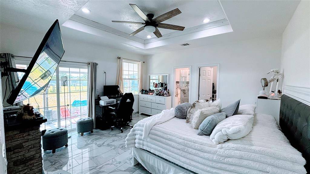 Master  bedroom features a cozy, modern design. The room is filled with natural light from the sliding glass doors leading to a patio. It includes a stylish ceiling fan, sleek tile flooring, and a dedicated workspace. The en-suite bathroom and ample storage enhance the room's functionality.