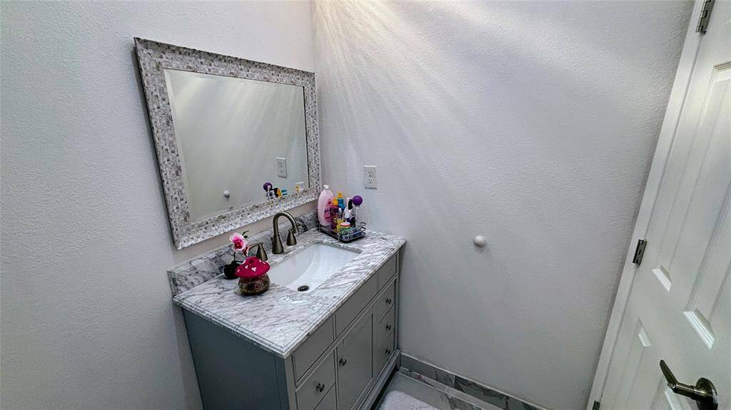 Modern bathroom with a marble-topped vanity and a decorative mirror. The space is compact with white walls and a tiled floor.