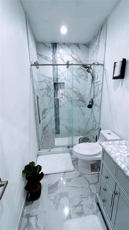 This modern bathroom features a sleek design with marble-style tiles, a glass-enclosed shower, and a vanity with a marble countertop.
