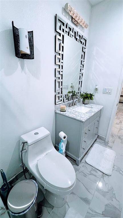 This modern bathroom features sleek white marble flooring, a contemporary vanity with a stylish geometric mirror, and a compact toilet. The space is well-lit, with elegant fixtures and a clean, minimalist design.