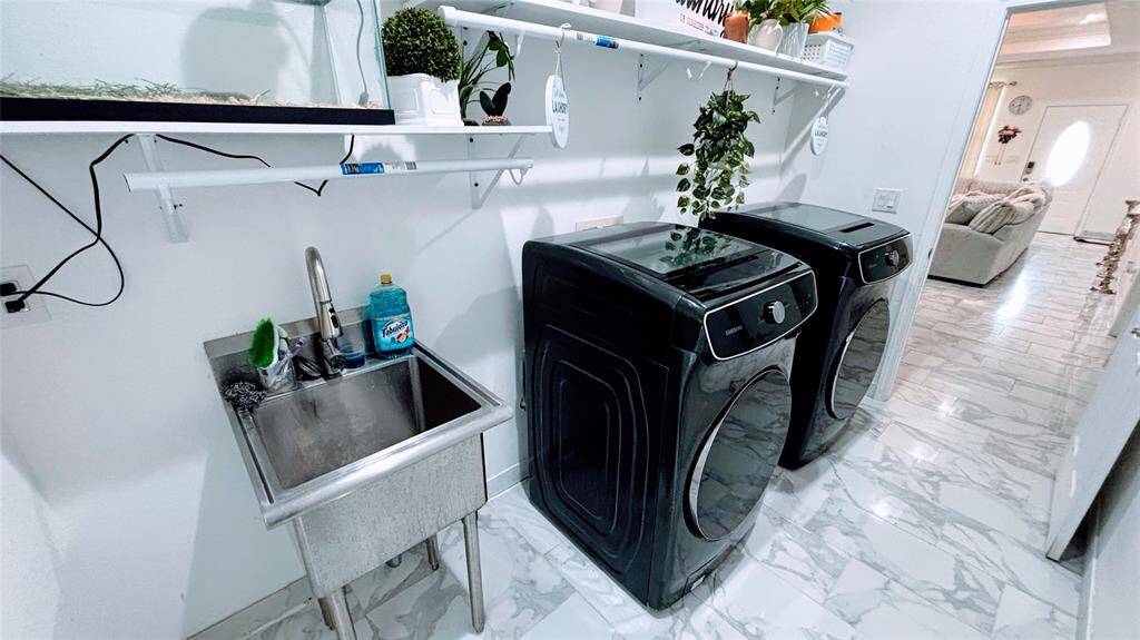 This photo showcases a modern laundry room with sleek black  and white shelving. The space is bright with marble-patterned flooring and opens into a cozy living area.