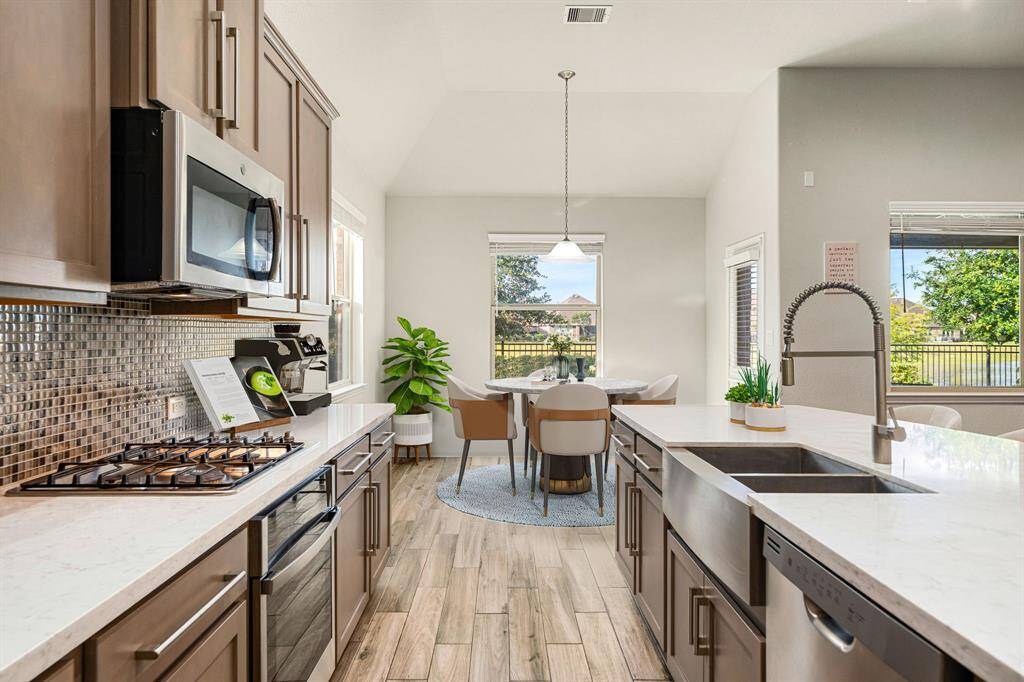 This beautifully designed kitchen features modern finishes, including sleek quartz countertops, a spacious farmhouse sink, and a stylish tile backsplash. Stainless steel appliances and ample cabinetry provide both functionality and elegance. The open layout seamlessly connects to the dining area, offering abundant natural light and a welcoming atmosphere perfect for everyday living and entertaining.