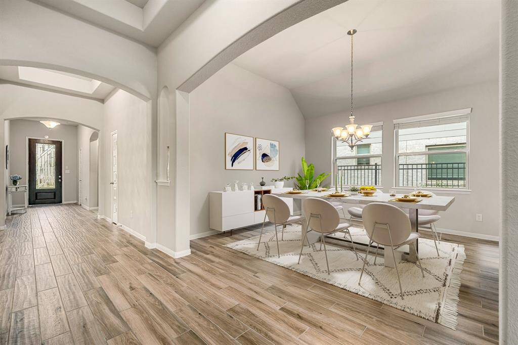 Step into this inviting space featuring soaring ceilings, elegant archways, and abundant natural light. The entryway flows seamlessly into a spacious formal dining area, accented by large windows and a classic chandelier. Warm wood-look tile flooring extends throughout, offering both style and durability in this beautifully designed layout.
