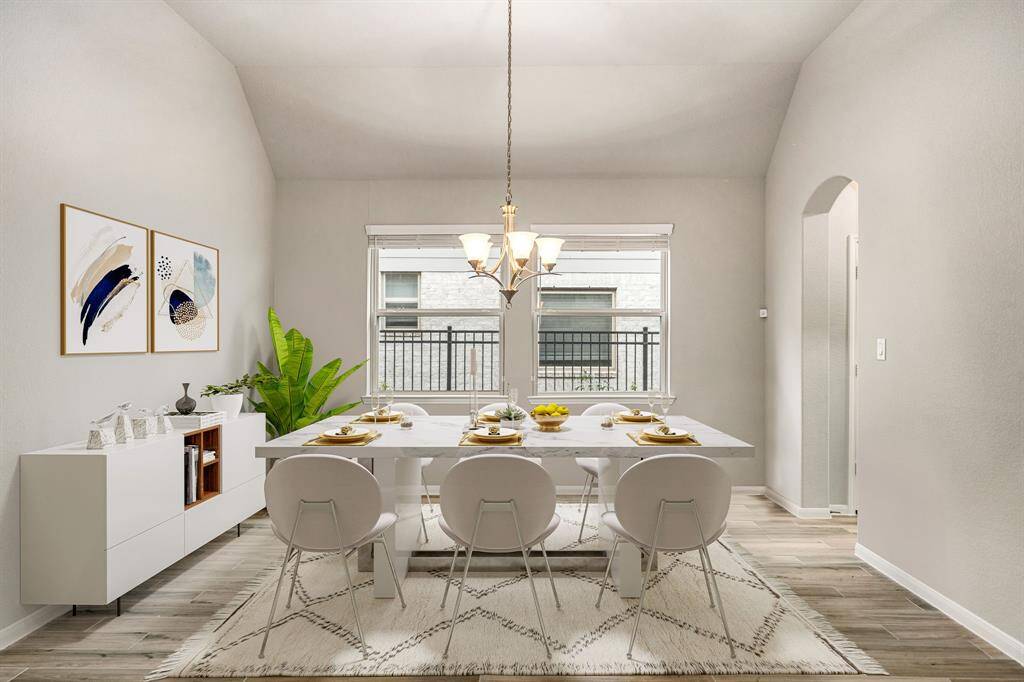This elegant dining area is filled with natural light from large, double windows and features a soaring vaulted ceiling that enhances the sense of space. Soft neutral tones and wood-look tile flooring create a warm and inviting atmosphere, while a classic chandelier adds a touch of sophistication. Perfectly positioned off the main living areas for seamless entertaining.