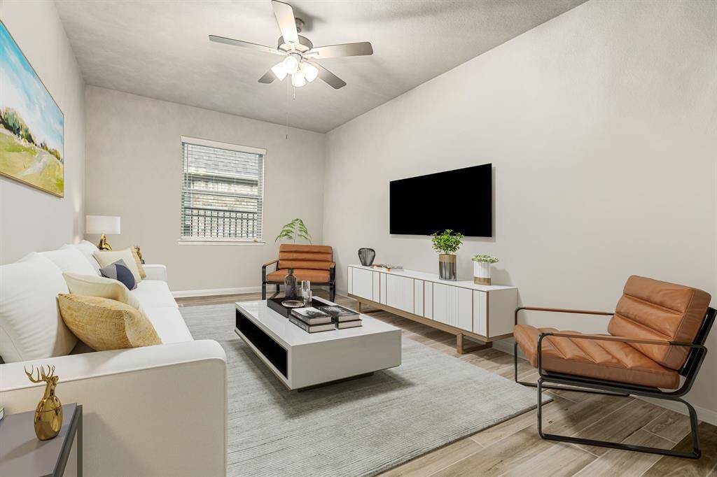 This inviting formal living room features ample natural light from a large window, complemented by sleek wood-style flooring and neutral wall tones that create a warm and modern atmosphere. A ceiling fan with overhead lighting adds both comfort and functionality. The spacious layout offers versatile design options, ideal for relaxation or entertaining guests.