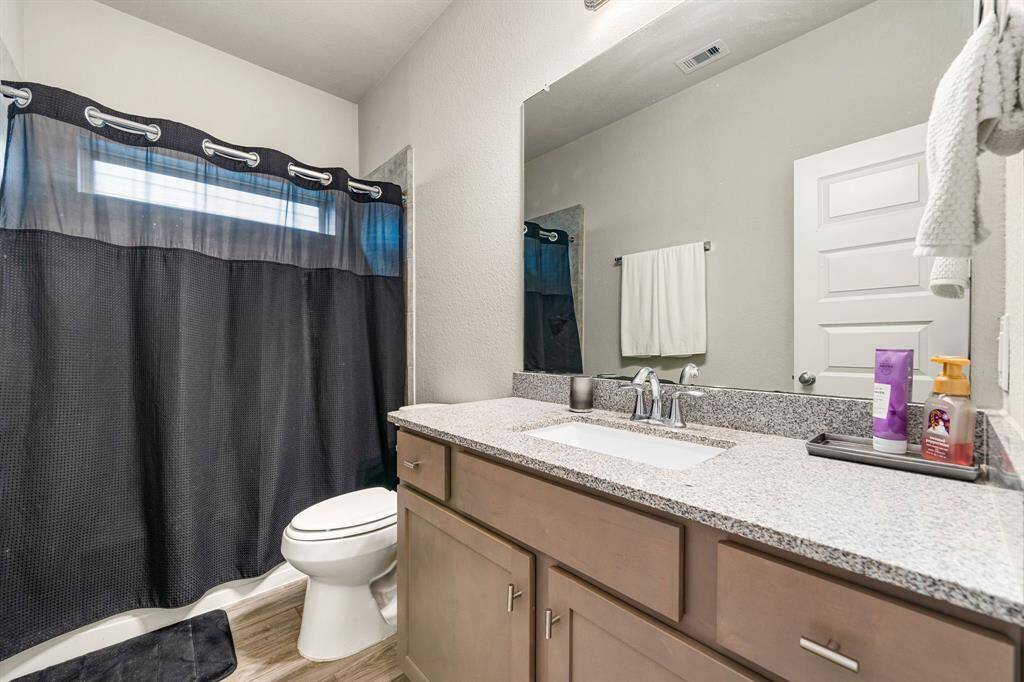 Secondary bathroom features Granite countertops and light cabinets, neutral paint, shower/tub combo with tile surround, large mirror, wood look tile floors, sleek fixtures and modern finishes, plenty of space to accommodate any visiting family or guests.