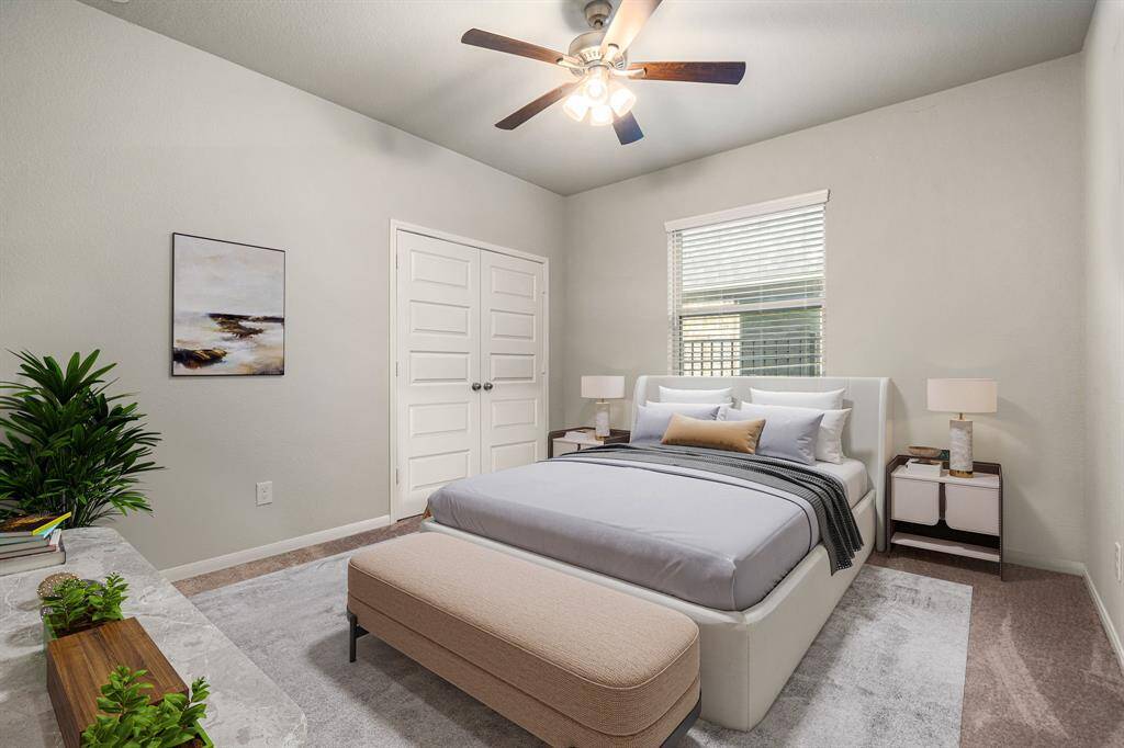 Secondary bedroom features plush carpet, neutral paint, dark stained ceiling fan with lighting and a large window with privacy blinds.