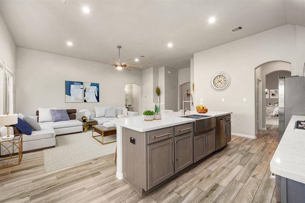This beautifully designed open-concept space features elegant wood-look tile flooring, high ceilings, and a seamless flow from the kitchen to the living area. The gourmet kitchen includes a large island with upgraded cabinetry, Quartz countertops, a deep farmhouse sink, and a high-arc faucet—ideal for both cooking and entertaining. Arched entryways and recessed lighting add a touch of sophistication throughout.