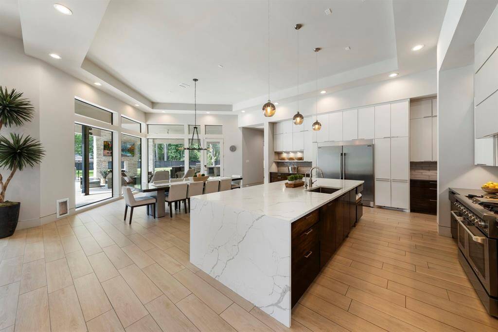 A gorgeous chef’s kitchen unfolds with dramatic waterfall Calacatta Laza countertops, sleek cabinetry, and floor-to-ceiling windows that flood the space with natural light and serene outdoor views.