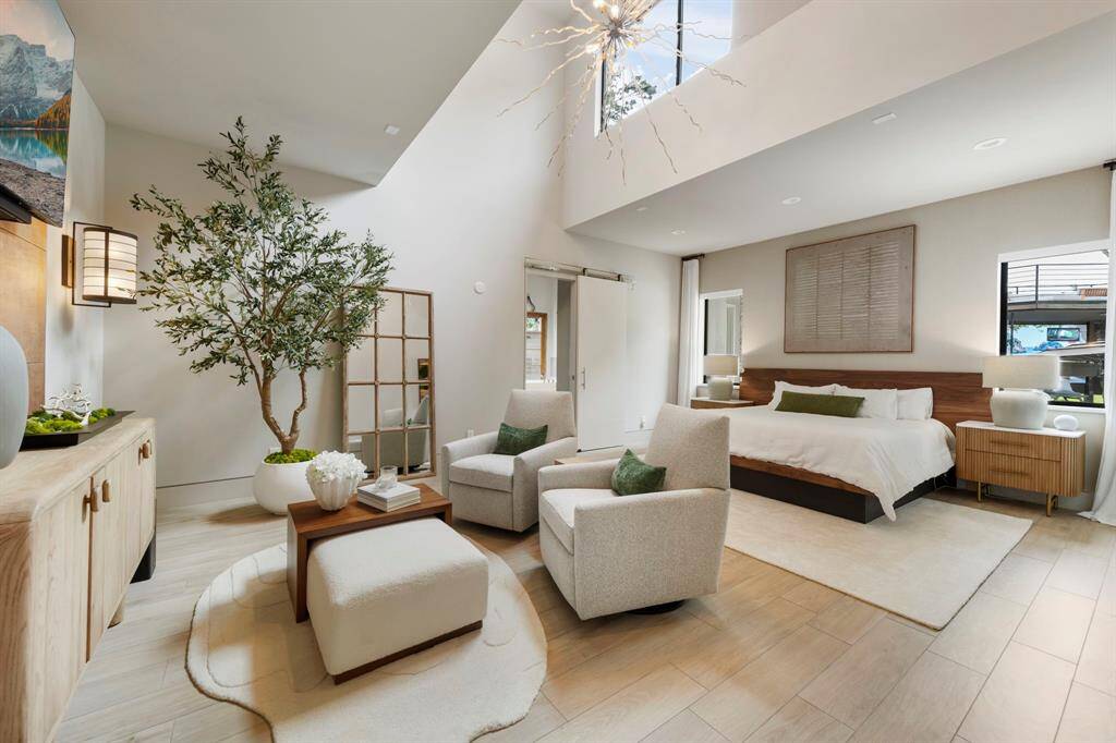 The serene primary suite features soaring ceilings, a dramatic statement chandelier, and a cozy sitting area that invites quiet mornings and restful nights.