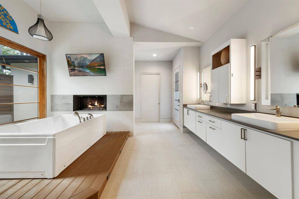 This elegant primary bath features dual vanities with sleek vessel sinks, a cozy fireplace above the soaking tub, and spa-inspired details designed for both beauty and serenity.