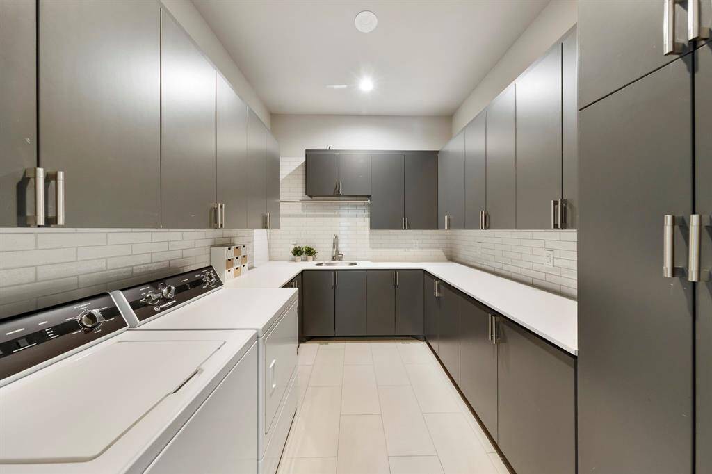 This sleek and spacious laundry room is designed for ultimate functionality, with abundant cabinetry, expansive countertops, and a clean modern aesthetic that makes everyday tasks feel effortless.