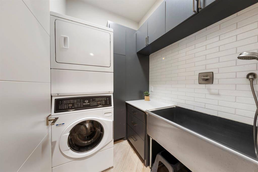 This compact yet highly functional laundry room features sleek cabinetry, a deep utility sink or pet washing station, and a stacked washer and dryer, ideal for streamlined everyday chores.
