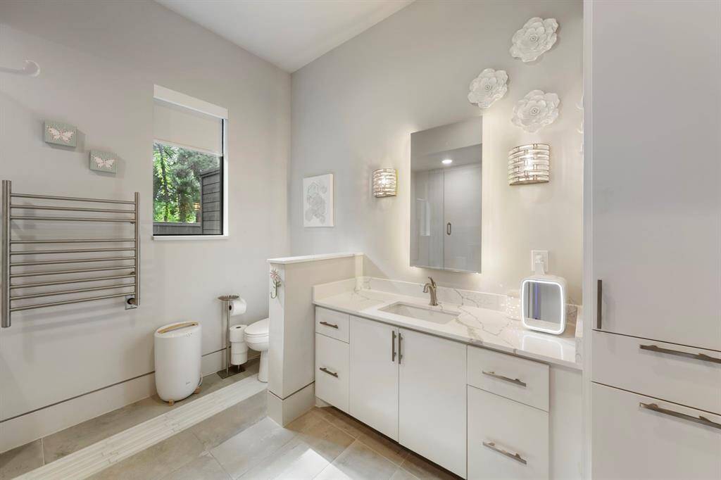 This serene en-suite bath showcases a soothing color palette, sleek countertops, generous storage, and a stylish shower/tub combination.