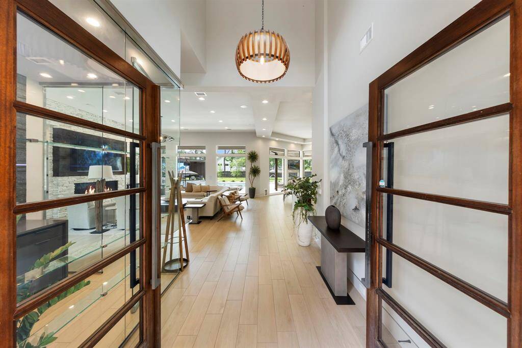 A stunning entryway framed by rich wood and glass doors opens into a luminous, contemporary interior filled with natural light, clean lines, and curated design.
