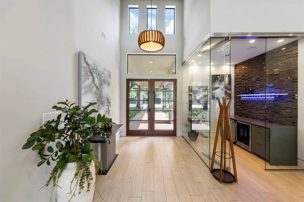 This soaring foyer bathed in natural light showcases a sleek, glass-enclosed modern wine bar that sets an elegant tone upon entry.