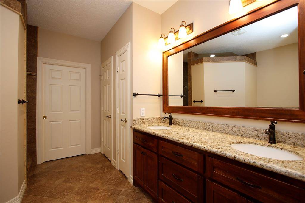 Primary bathroom features dual-sink vanity with granite countertops and continues the elegant dark wood cabinets. Storage closet, private water closet and primary closet to the back of bathroom.