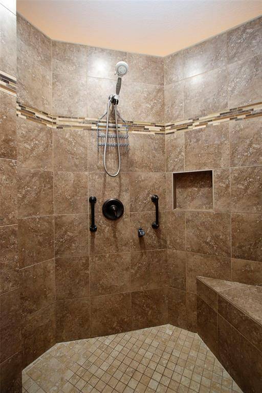 Spacious tile shower with decorative detail, large built-in bench, handheld showerhead and safety handles for added comfort and accessibility.