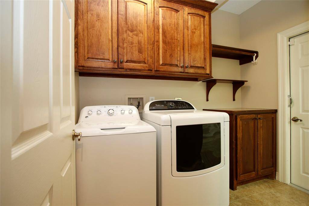 This laundry room features a washer and dryer set and beautiful cabinets and shelving.  Laundry room sits just off the kitchen and can also be accessed through the 3-car garage.