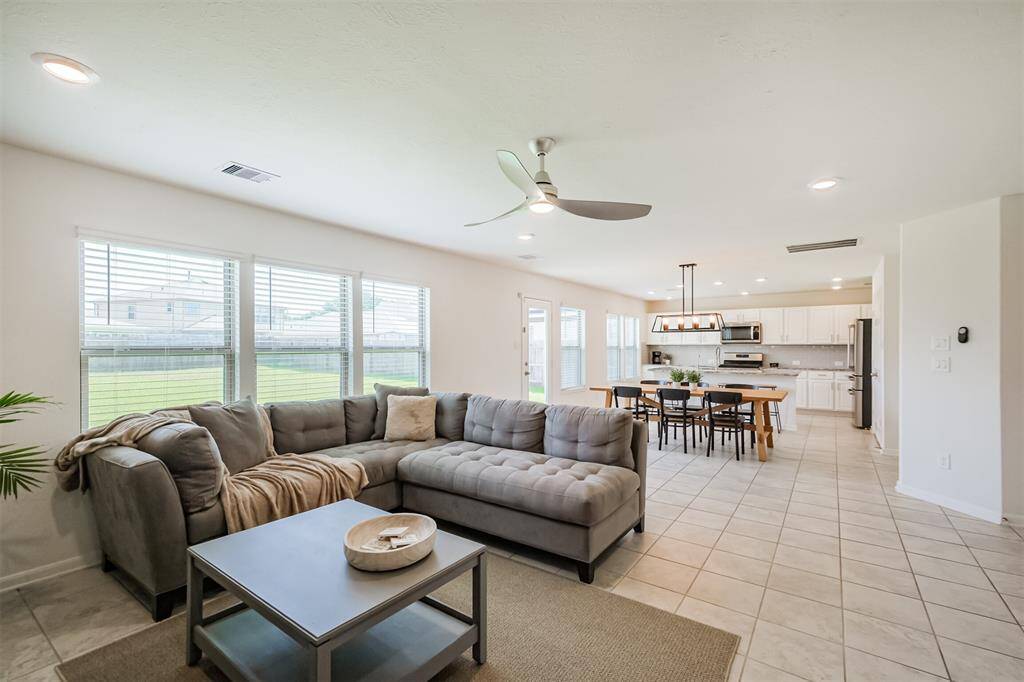 The spacious, open-concept living area provides ample natural light. The adjacent dining area and kitchen boast stylish lighting, white cabinetry, and stainless steel appliances.
