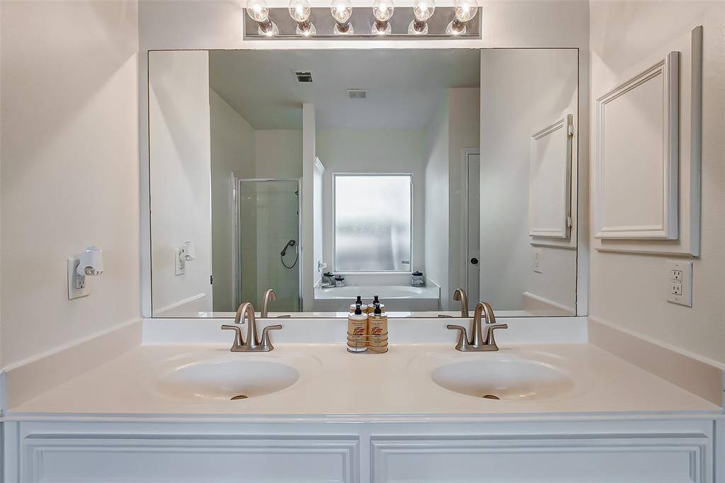 The bathroom features a spacious dual sink vanity with a large frameless mirror and vanity lighting overhead, offering both style and functionality. Ample storage is provided by cabinets below, keeping the space organized and clutter-free.