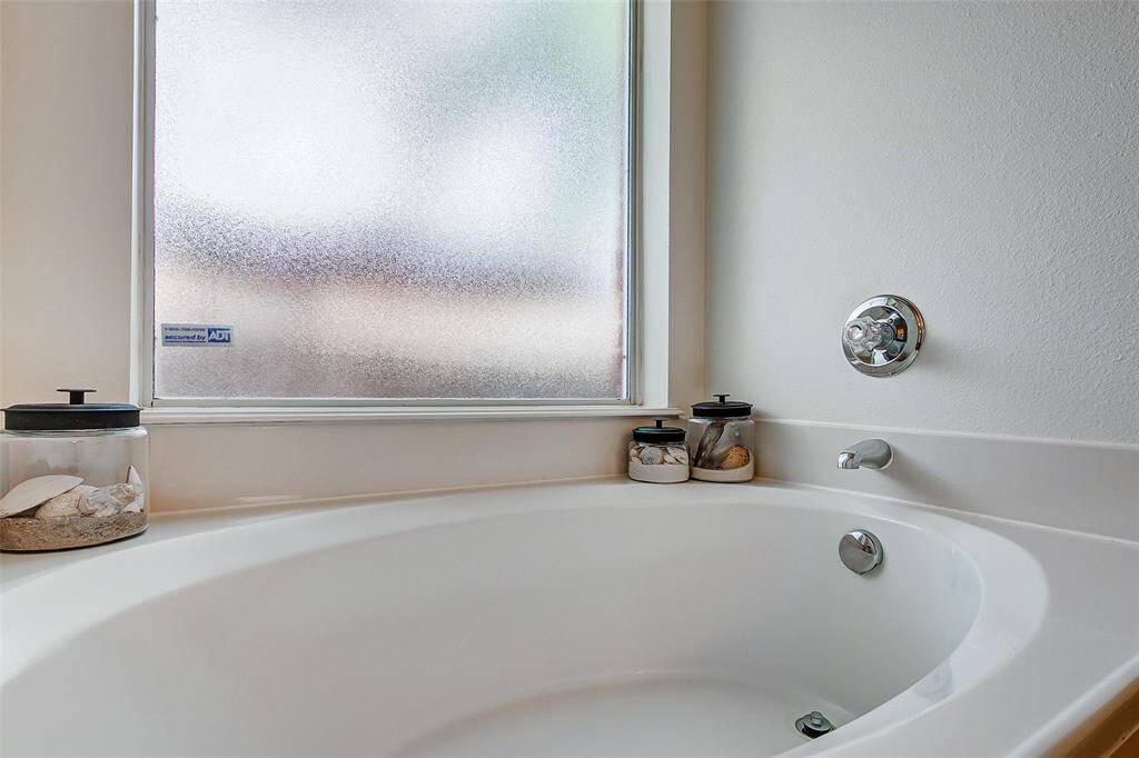 The generously sized garden tub is positioned beneath a large frosted glass window, allowing ample natural light to fill the space while maintaining privacy, creating a perfect balance of brightness and seclusion.