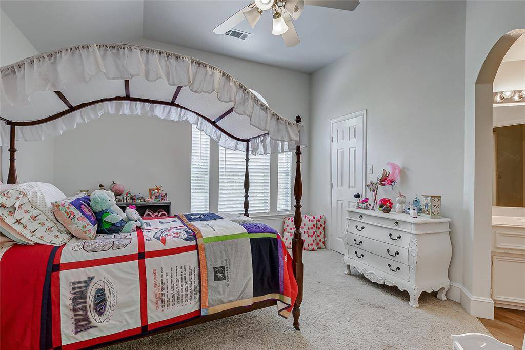 The first secondary bedroom features generous space, a vaulted ceiling with a fan, large windows with sidelight and sunburst accents, and plush carpeting. It shares a bathroom with the game room, making it a perfect retreat for guests.