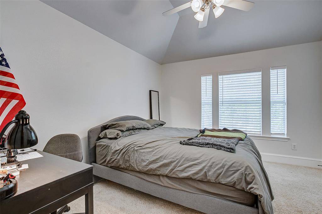 The second of three secondary bedrooms offers ample space, a high vaulted ceiling with a fan, and a large window with sidelight windows that flood the room with natural light. Plush carpeting adds warmth, creating a cozy retreat. This bedroom also shares a Jack-and-Jill bathroom.