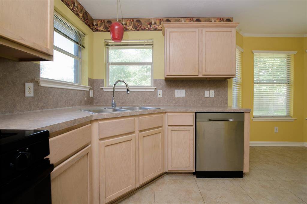 A closer look at the double-basin sink and dishwasher setup in this bright kitchen corner. Light wood cabinets, durable counters, and tile backsplash add both charm and utility. Positioned between two windows, this space is perfect for enjoying backyard views while prepping meals or washing up.