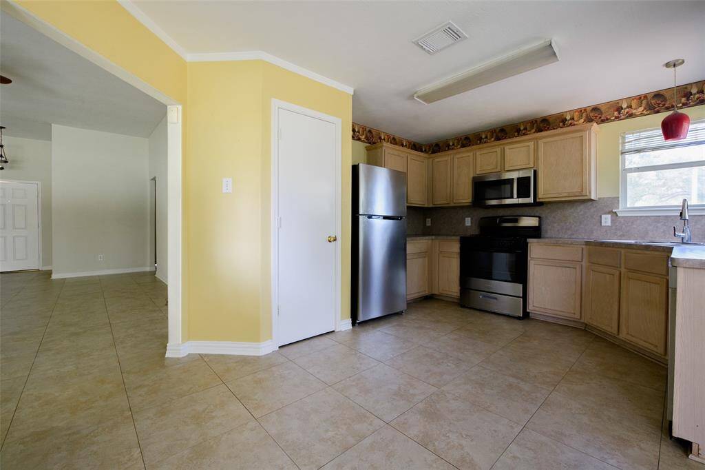 Enjoy a seamless flow from the kitchen to the living area in this open-concept layout. The pantry offers generous storage, while the adjacent stainless steel refrigerator and full tile floors deliver easy maintenance and modern appeal. Bright, open, and functional for everyday living.