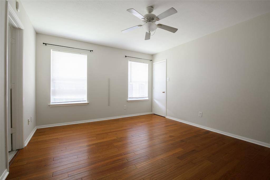 The primary bedroom features rich hardwood floors, soft natural light from two large windows, neutral walls, and a ceiling fan for added comfort. With direct access to the en-suite bath and walk-in closet, this serene space is perfect for relaxing and recharging at the end of the day.