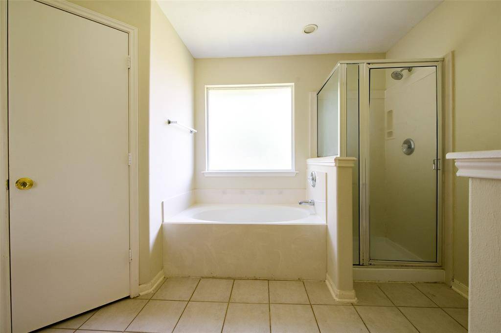 The primary bathroom offers a relaxing garden tub and separate walk-in shower, ideal for unwinding after a long day. A frosted privacy window brings in soft natural light, enhancing the serene atmosphere. Clean tile floors and soft neutral tones complete the spa-like feel.