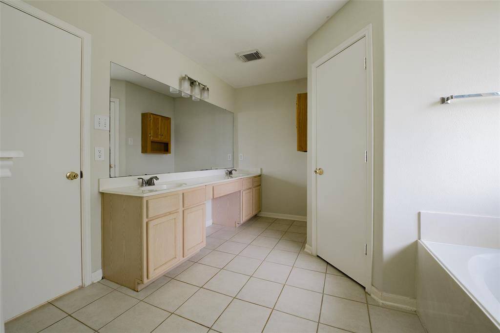 The dual-sink vanity in the primary bath features ample counter space, light wood cabinetry, and a full-length mirror—perfect for busy mornings or shared routines. Wall-mounted lighting and generous storage make this bathroom both functional and inviting.