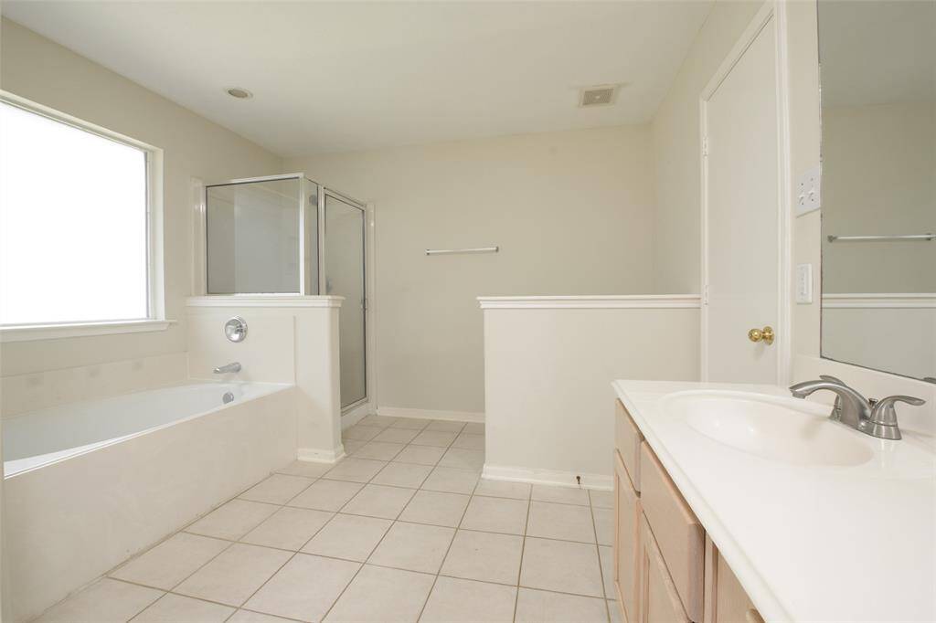 A broader perspective of the primary bathroom reveals its open layout with double vanities, a soaking tub, and glass-enclosed shower. The generous footprint allows for easy movement, while neutral tiles and paint create a calm, cohesive space.