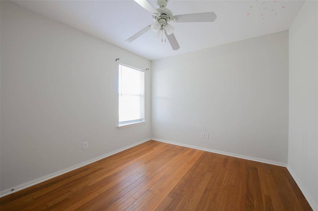 This secondary bedroom features warm wood floors, a ceiling fan, and a large window that fills the room with natural light. Its simple, neutral palette and cozy size make it versatile—ideal for a guest room, nursery, or home office.