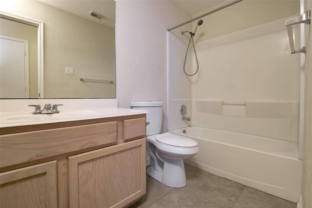 This full guest bathroom offers functionality and comfort with a tub/shower combo, single-sink vanity, and expansive wall mirror. Neutral finishes, including ceramic tile flooring and a modern handheld showerhead, provide ease of maintenance and timeless appeal for guests or family use.