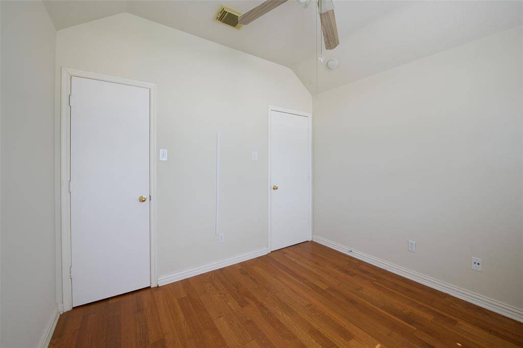 A second view of the third bedroom highlights its vaulted ceiling, ceiling fan, and dual closets—ideal for storage or shared use. The crisp white trim and hardwood-style floors give the room a fresh, open feel perfect for a range of uses.