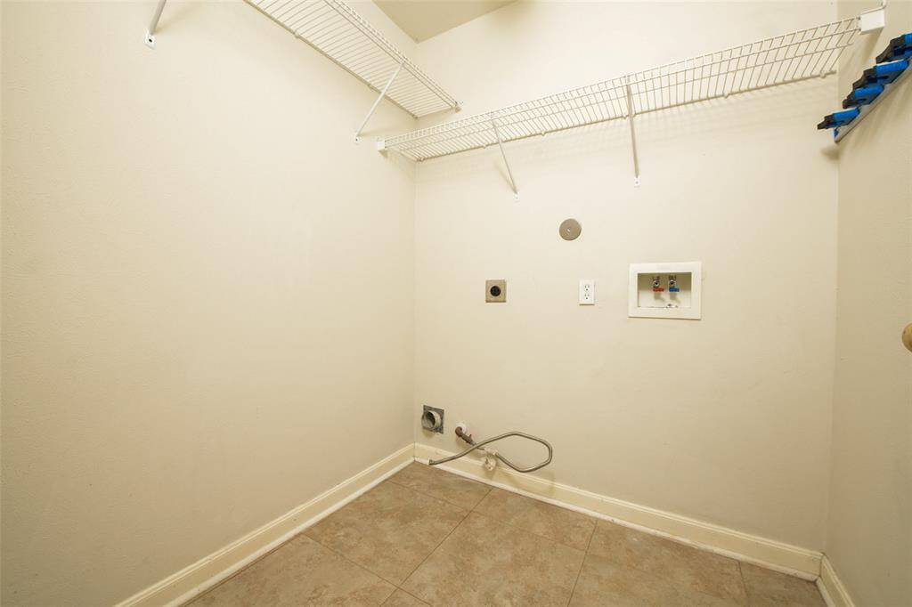 Conveniently located utility room includes washer and dryer hookups, upper shelving for organization, and easy-clean tile flooring. A clean and functional space, perfect for keeping laundry tucked away and out of sight, while still accessible just off the main living areas.