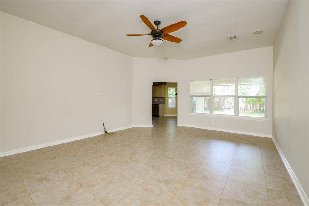 Spacious and bright, the living room features neutral tile flooring, high ceilings, and a ceiling fan for added comfort. Large windows offer a beautiful view of the backyard and flood the space with natural light, creating an inviting spot for everyday living or entertaining.