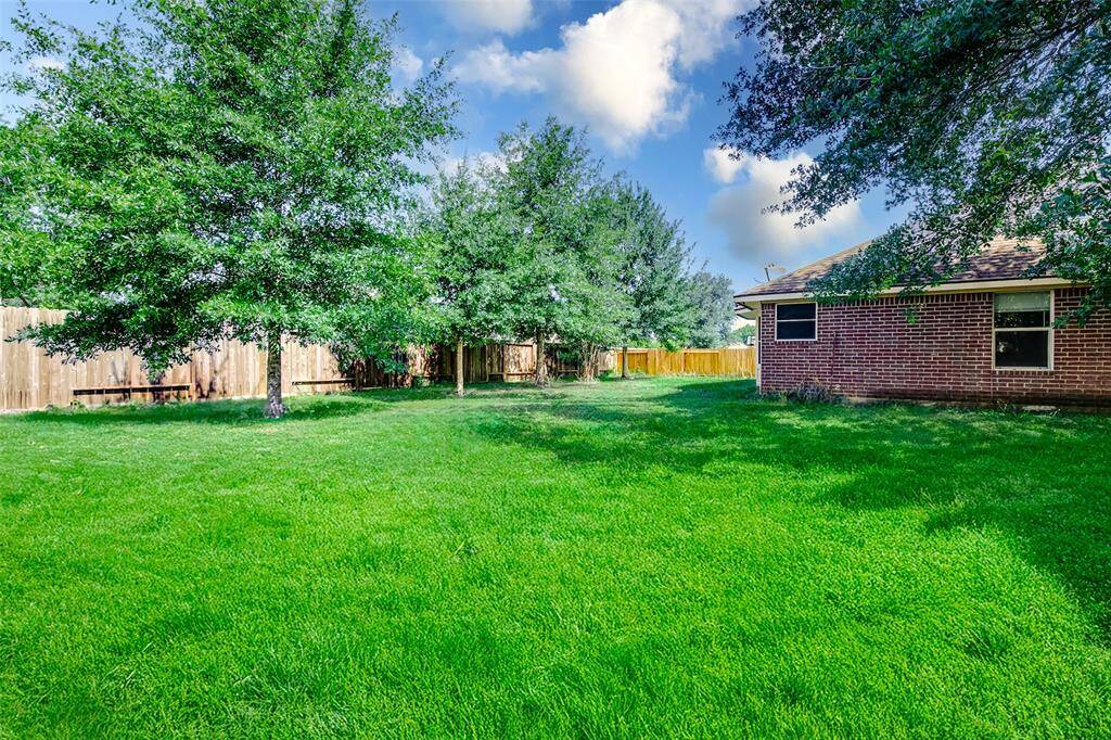 A lush green lawn stretches across this expansive backyard, offering endless possibilities for outdoor fun. Mature trees provide shade and privacy along the wooden fence line, while the red brick exterior adds charm and durability to the rear of the home.