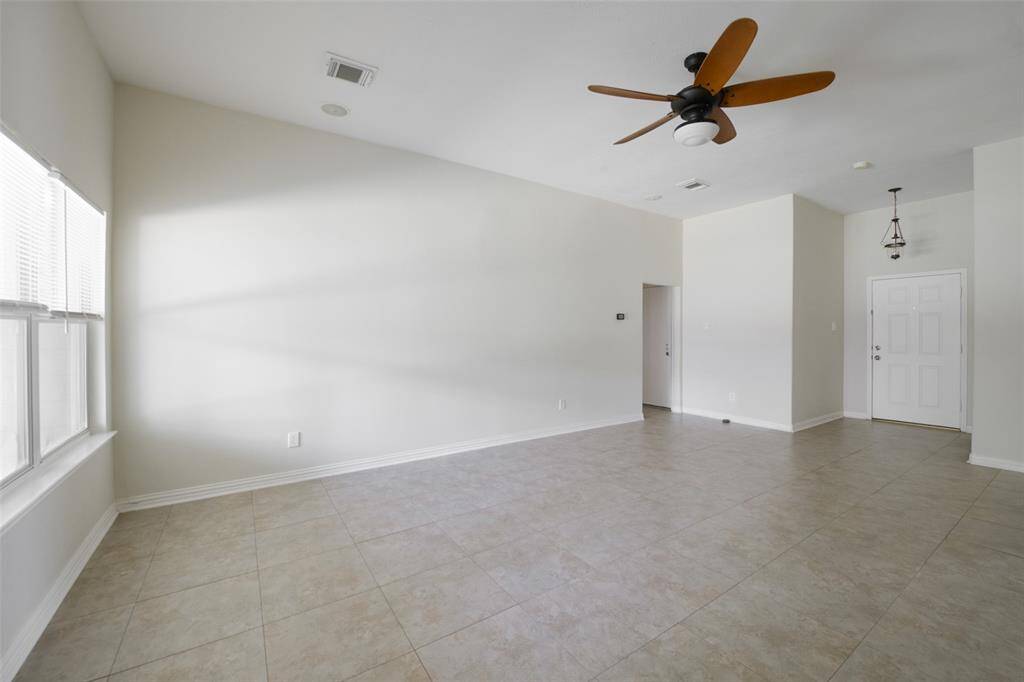 This wide-open living area is the central hub of the home, featuring tile flooring, fresh neutral walls, and a sleek ceiling fan. With sightlines to the front entry and connecting hallways, this space is both functional and welcoming for guests and gatherings.