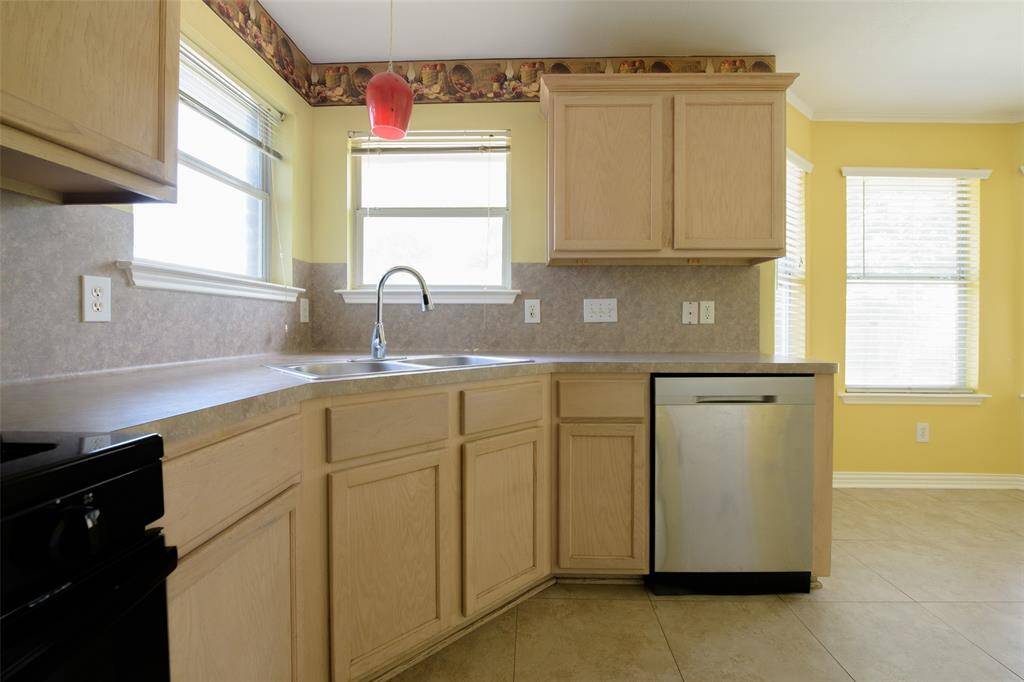 The kitchen offers generous counter space, dual-basin sink, and abundant cabinetry with a charming wraparound layout. Natural light pours in through two windows, while the decorative border trim adds a playful touch. Stainless steel appliances complete the look.