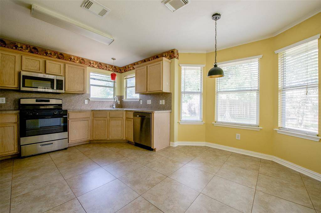 This open kitchen and breakfast space is the heart of the home, offering natural light from multiple windows, spacious tile flooring, and plenty of room for casual dining. The stainless steel appliances and extended countertop space provide functionality and style, ideal for everyday meals or entertaining.