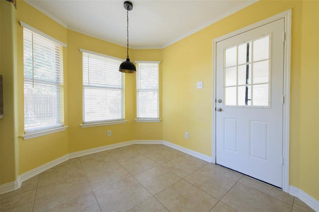 This bright and cheerful breakfast nook is surrounded by windows that flood the space with natural light. Neutral tile floors and fresh yellow walls make the space pop, while the glass-paned door offers quick access to the covered patio and backyard for seamless indoor-outdoor living.