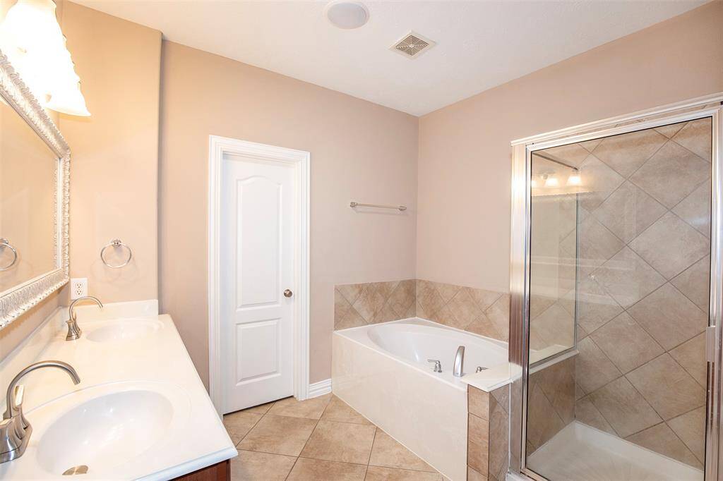 The primary bathroom offers a spa-like atmosphere with a tiled shower, a relaxing garden tub, and a large vanity featuring dual sinks.