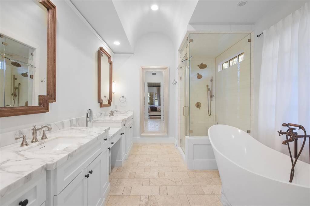 The primary bathroom is a luxurious sanctuary, designed with exquisite attention to detail. The arched ceiling adds architectural elegance, a sleek vessel tub rests as a statement piece, and a separate stand-up shower with frameless glass doors and gleaming tile work offers a spa-like experience. The double vanity with marble countertops, provides ample space for daily routines.