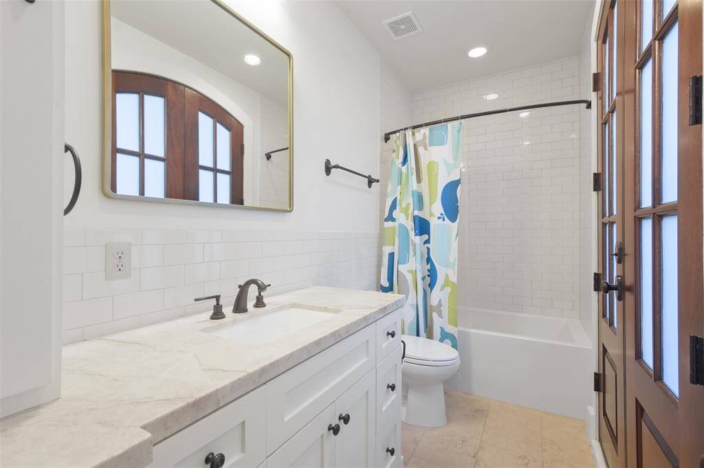 The secondary bathroom offers a tub and shower combo, featuring sleek tilework that extends from the tub to the ceiling with a marble counter, framed mirror and great storage.