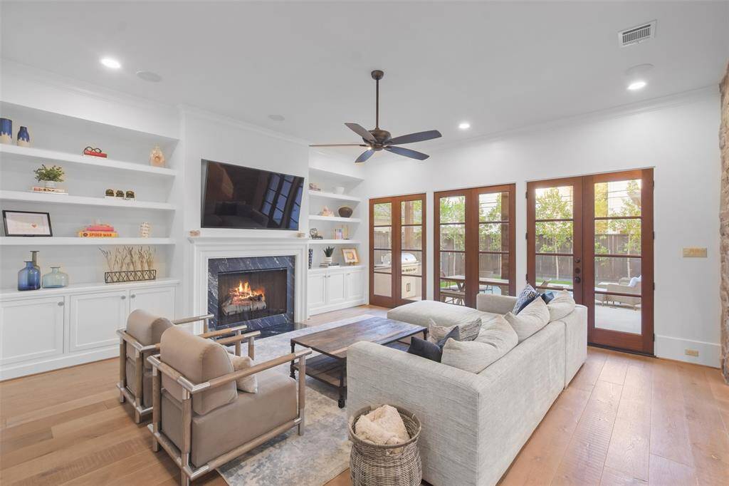 The family room is a harmonious blend of charm & functionality, with surround sound speakers and anchored by a stone surround fireplace. Flanking the fireplace are custom-built bookshelves, perfect for showcasing books, artful decor, & personal mementos, adding both style & practicality to the space. French doors open directly to the backyard, inviting natural light to stream in and offering a seamless connection to the outdoor living area making entertaining easy.