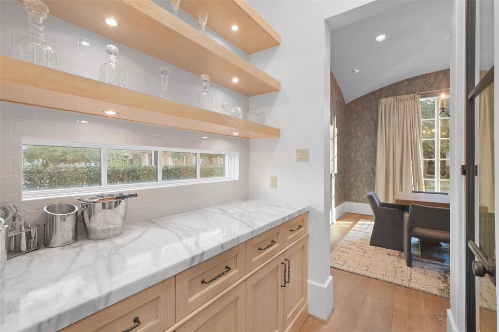 The butler's pantry serves as the perfect bridge between the formal dining room and the kitchen. Sleek floating shelves line the walls, providing open storage for elegant glassware, fine china, or decorative accents, with a marble countertop that offers a convenient surface for meal prep or staging dishes during dinner parties.